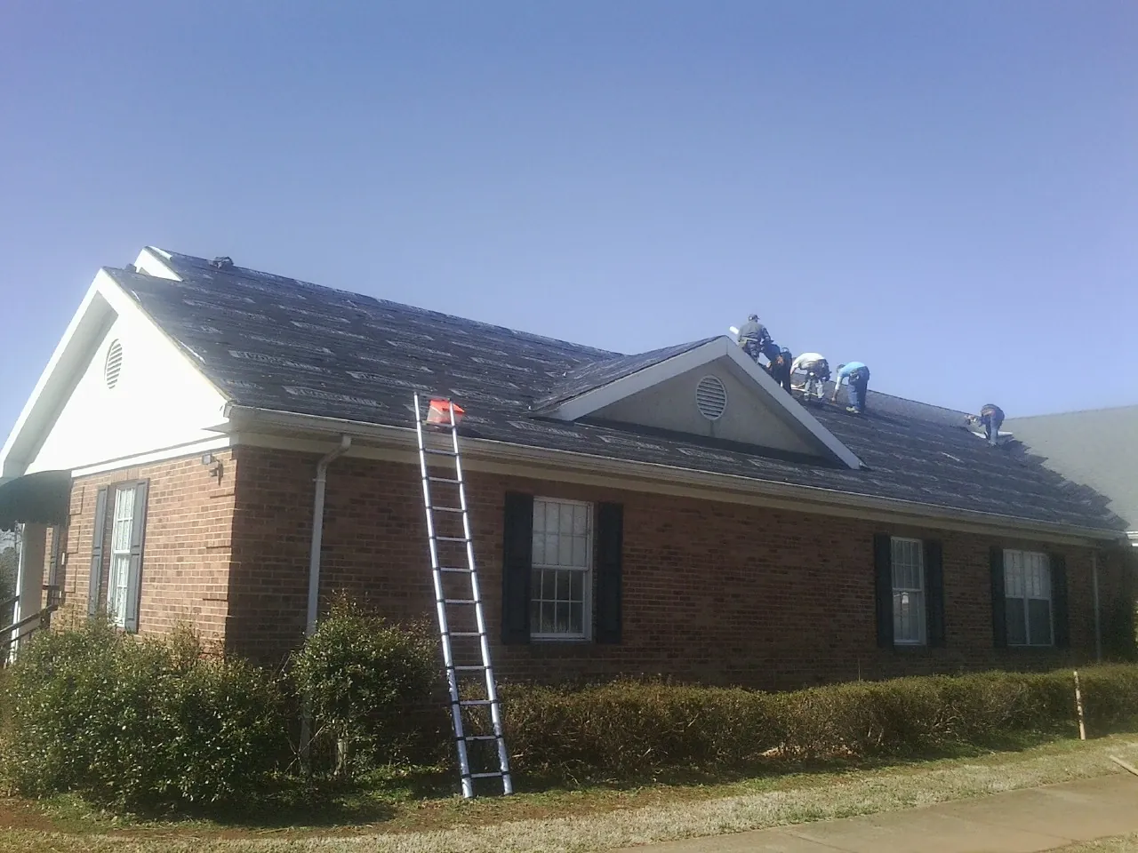Crew tearing shingles off a brick ranch roof with a ladder set — Emergency Roof Repair work by our crew in Red Wing