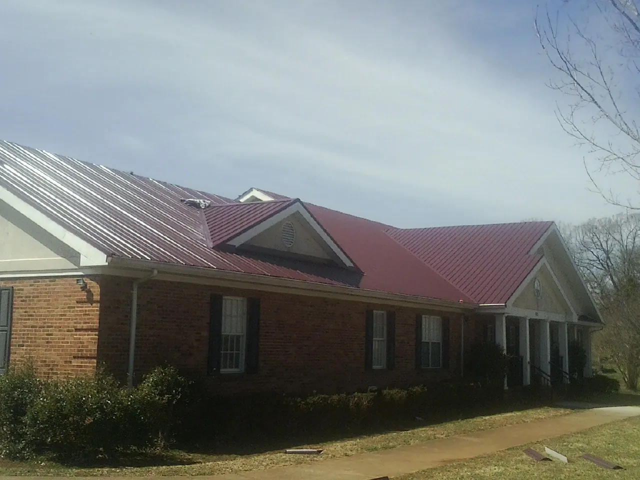Red metal roof with gabled entries on a long brick building, from a Hail Damage Roof Repair job in Red Wing