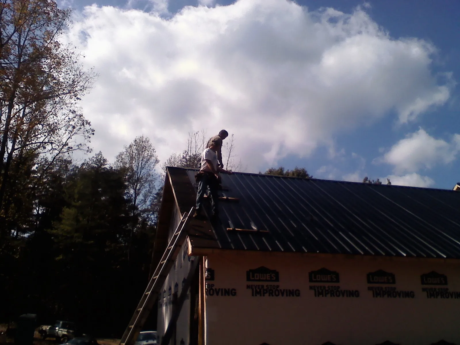 Roofer fastening dark metal panels high against a cloudy sky, from a Roof Inspection job in Red Wing