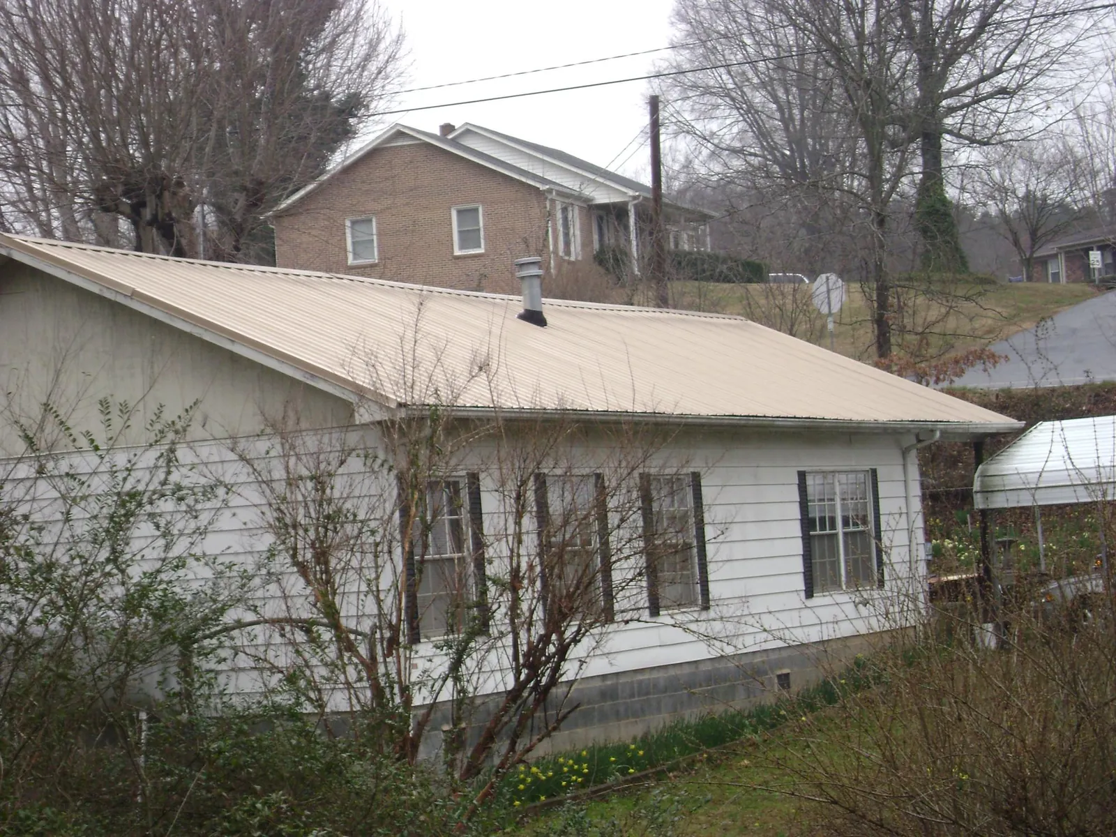 Tan metal roof on a white sided house set into a hillside — Commercial Roofing by Roofing Brothers in Red Wing